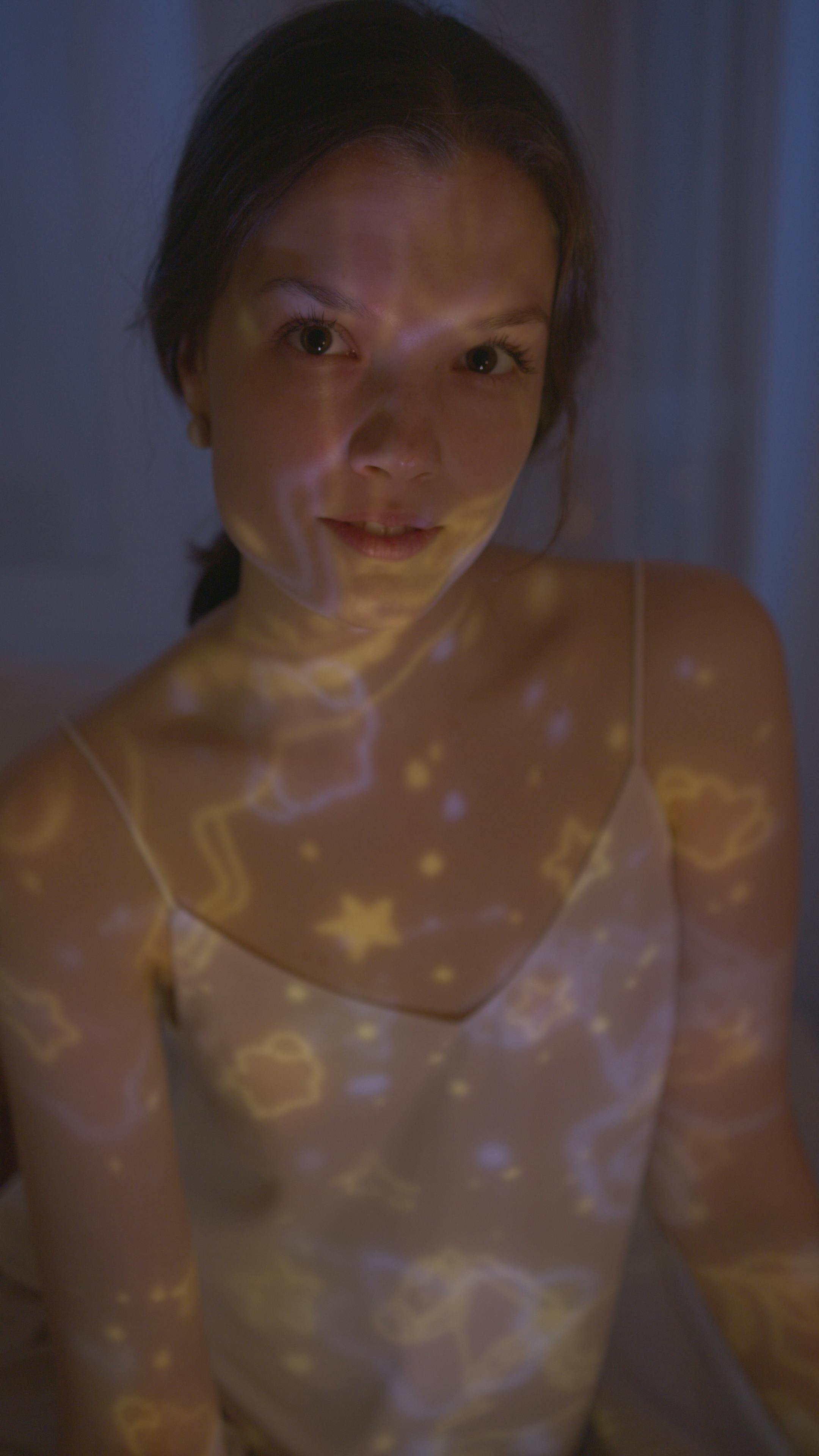 A child confidently holding a yoga tree pose in a dark room with blue ambient light.